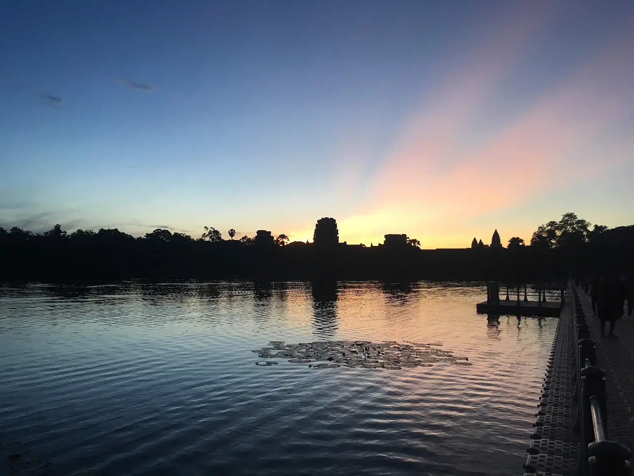 The towers of Angkor Wat in silhouette against a pink and blue dawn, reflected in the moat