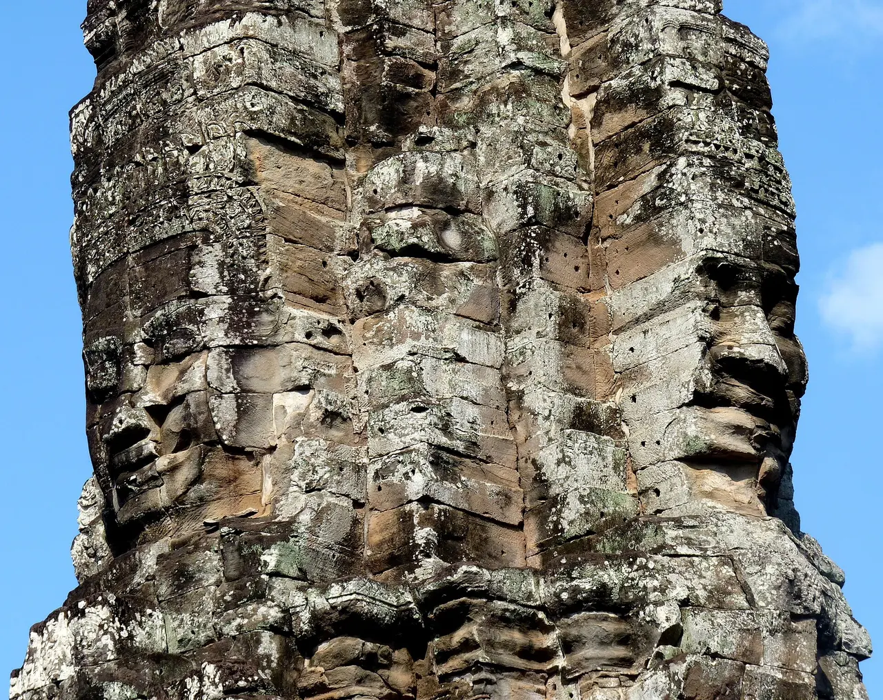 Huge serene stone faces carved into the towers of a temple against a blue sky