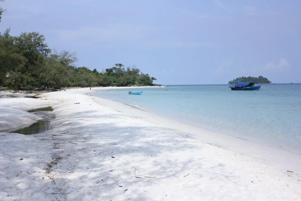 A white sand beach curving along clear turquoise water with a small island offshore