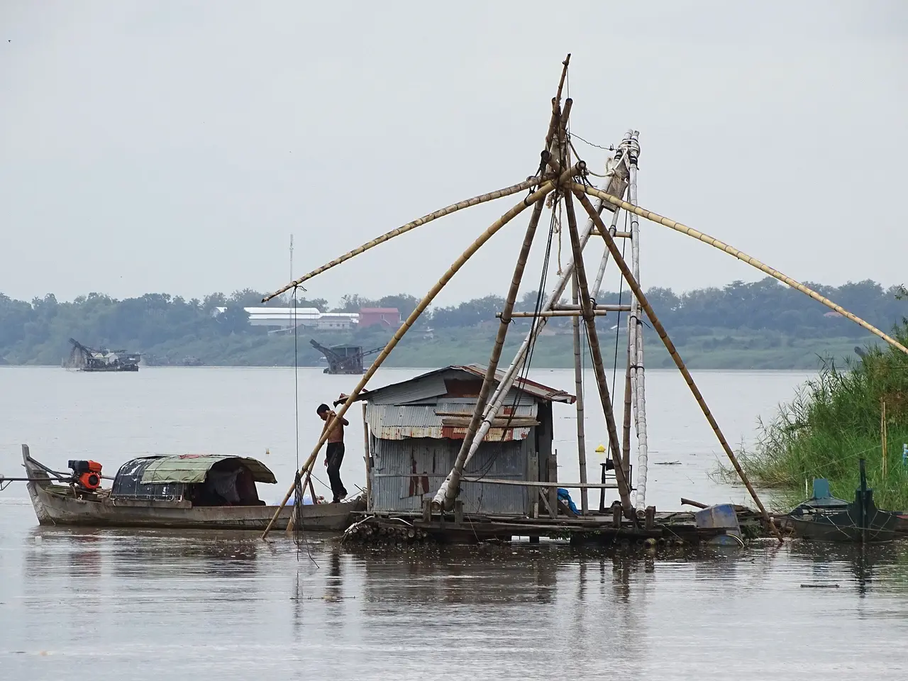 A wooden fishing platform with a large lift net beside a boat on the Mekong