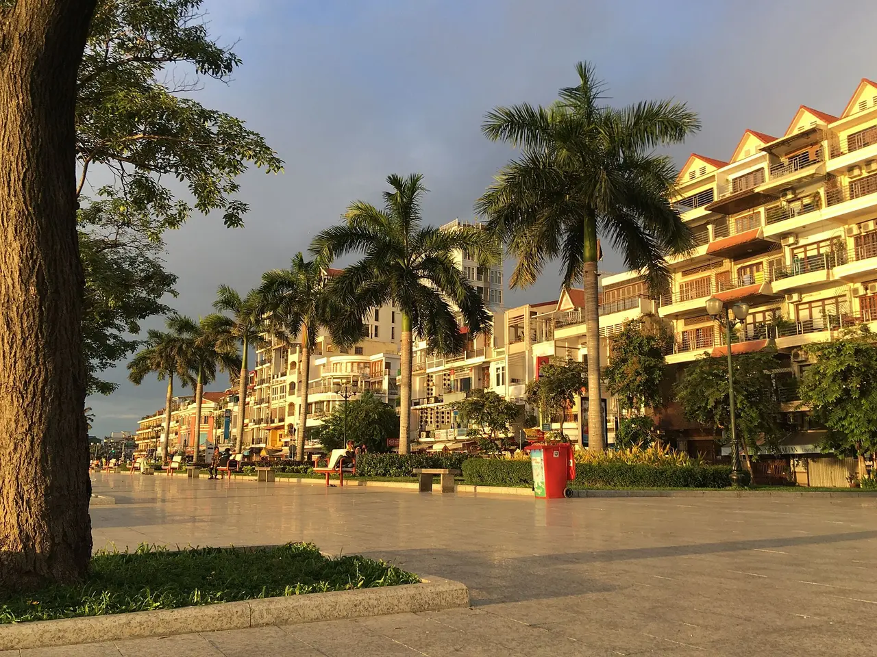 Palm-lined riverside promenade with low buildings in warm evening light