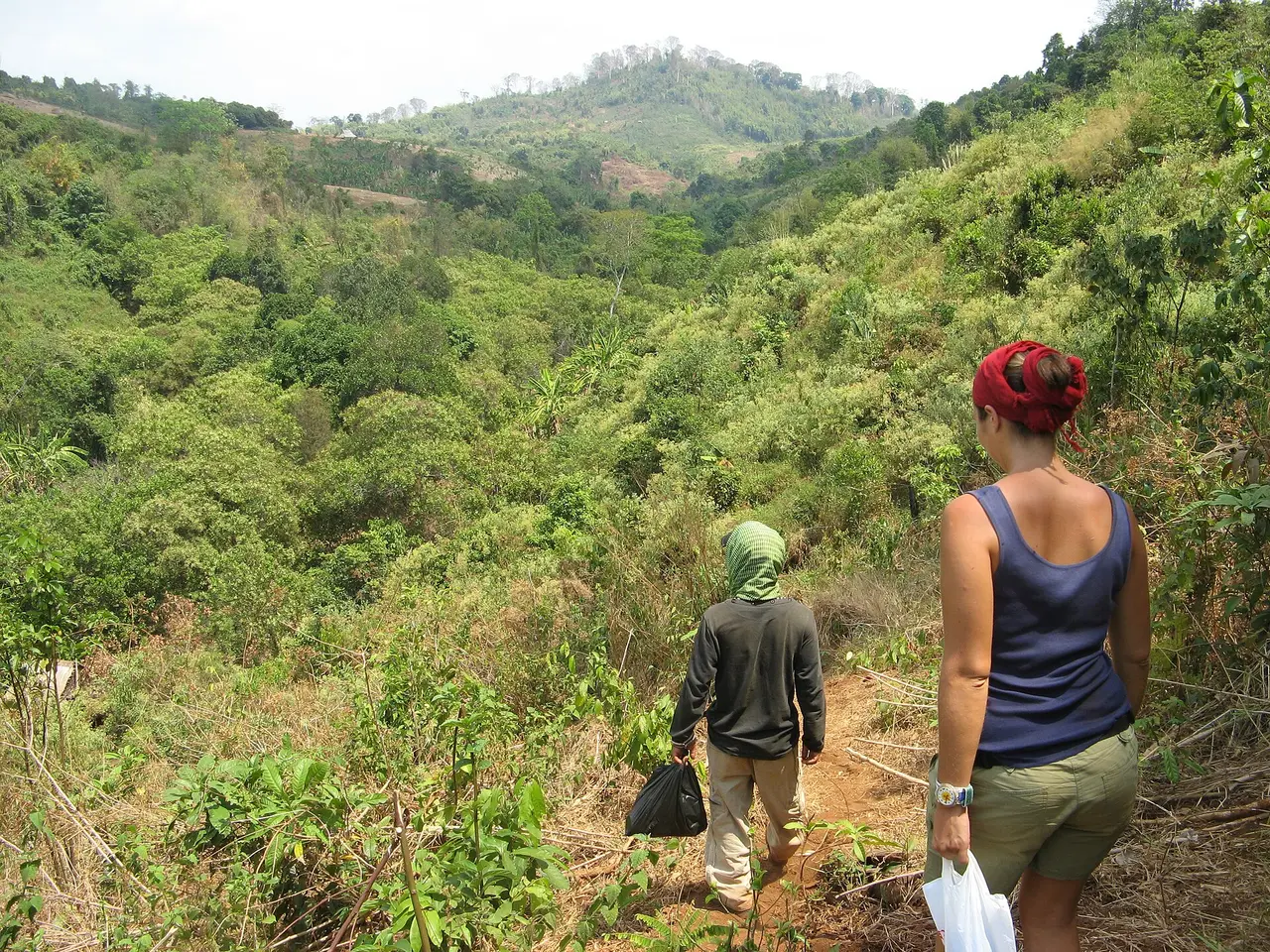 Two walkers seen from behind on a narrow red-earth path through green hills